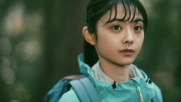The young woman in a teal jacket with a backpack in the woods