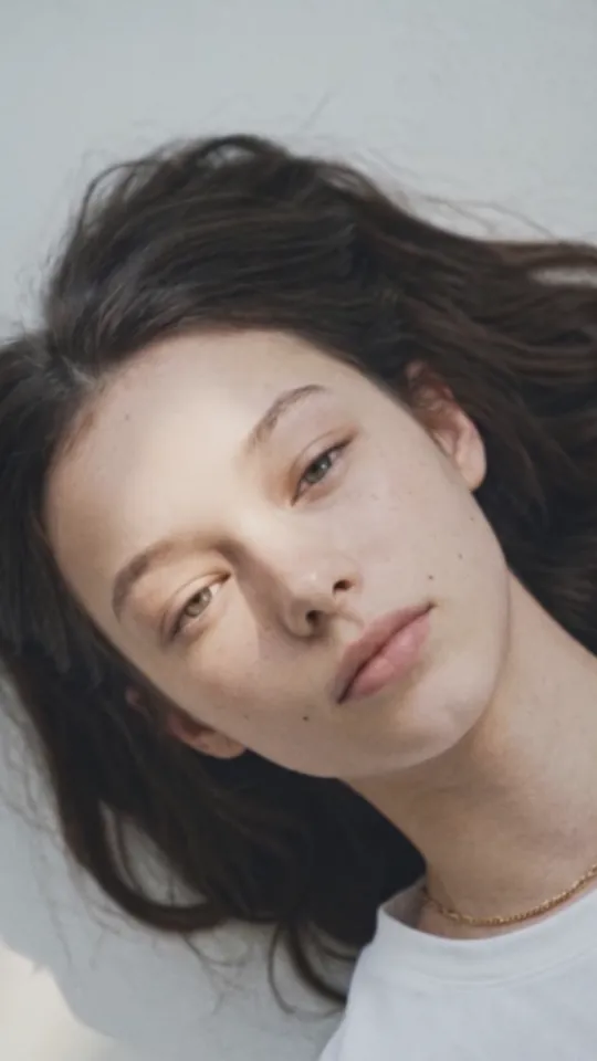 A woman lying back in soft light, in a white tee