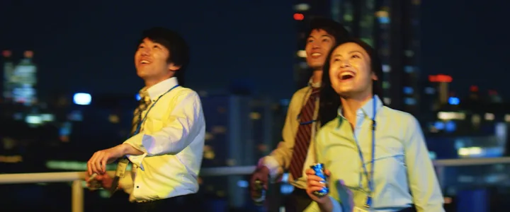 Colleagues toasting with KIRIN Fire cans on a night rooftop