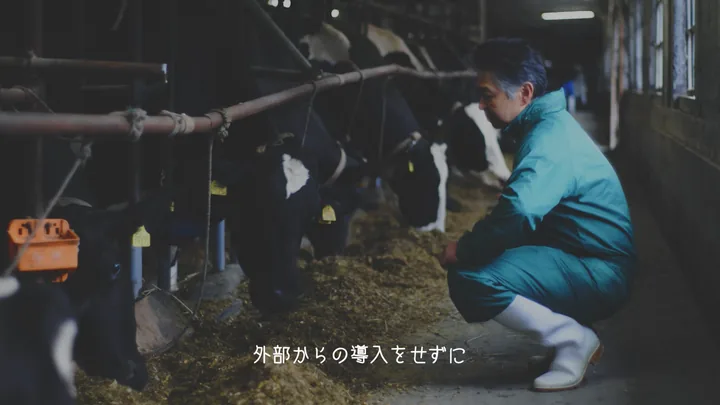 A farmer tending dairy cows in the barn — 「外部からの導入をせずに」