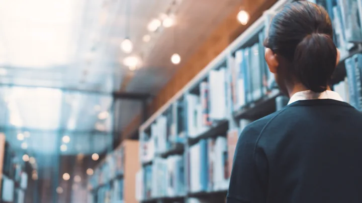 A woman seen from behind beside tall bookshelves in a lit library