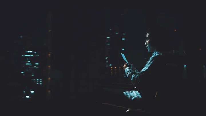 A person reading a glowing screen in the dark