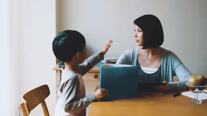 A mother and son at a table, the boy pointing at a book
