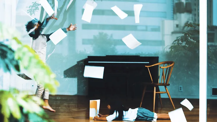 Sheets of paper flying around a girl lying on the floor by a piano