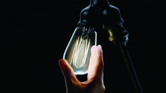 A hand turns a filament bulb in its socket until it glows