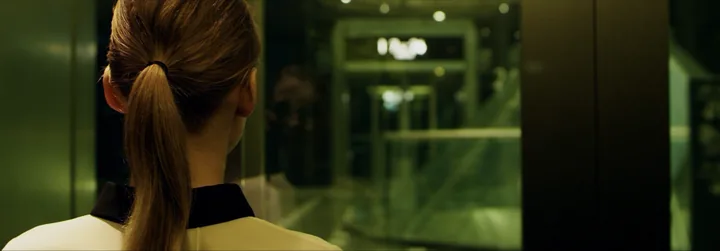 A woman with a ponytail facing a lit corridor