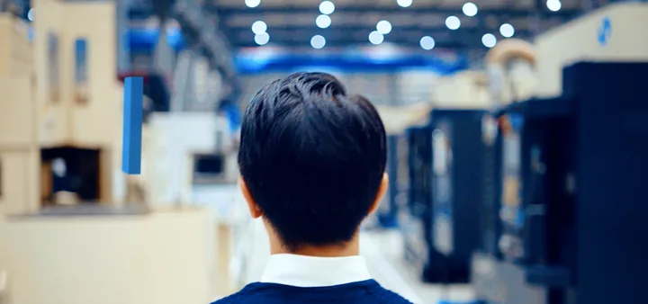 A worker seen from behind in a factory, SMFL mark in the air
