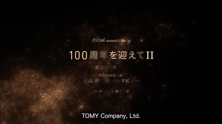 The title card 「100周年を迎えて II」 forming out of gold particles — TOMY Company, Ltd.