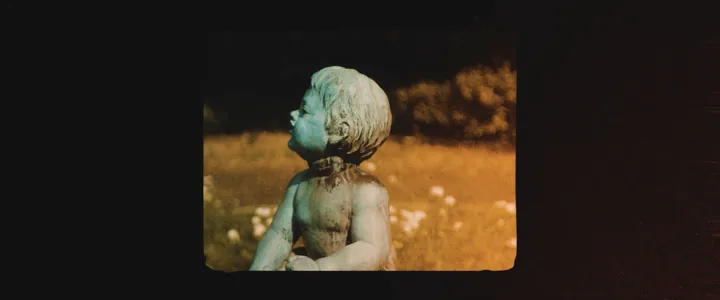 A statue in a field, framed like a film frame on black