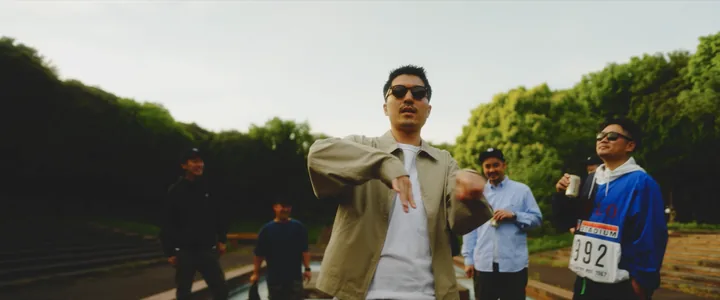 A rapper in sunglasses rhyming in front of the crew