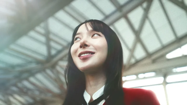 A woman in a red blazer looking up under a station roof