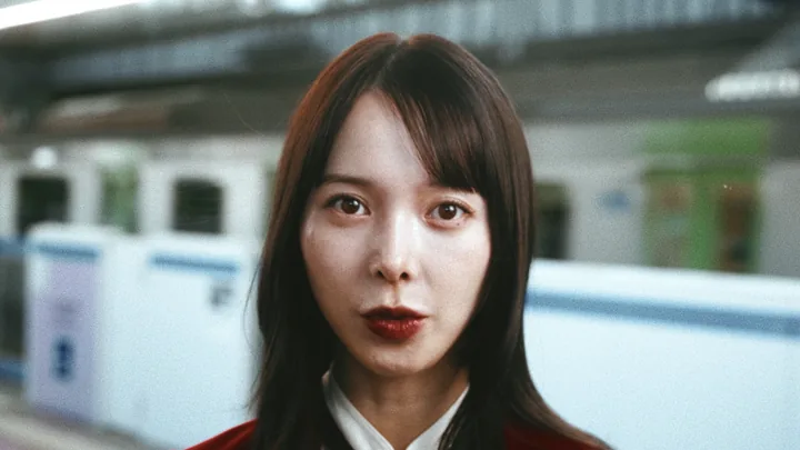 A woman in a red blazer on a train platform, facing the camera