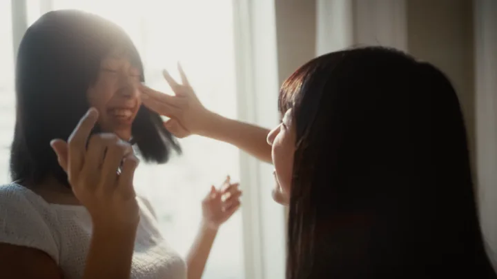 Two girls laughing, one touching the other's hair