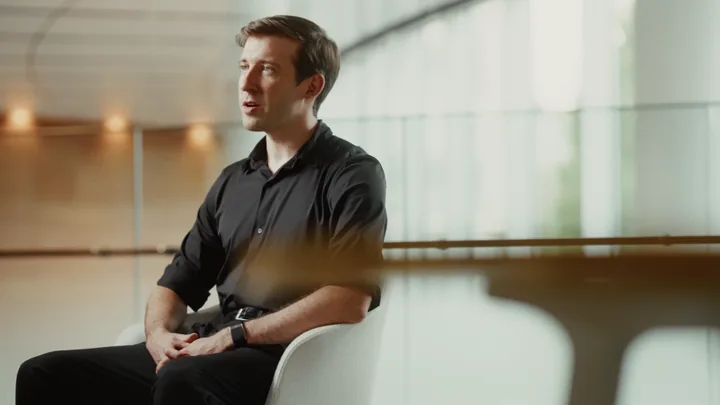 A man in a black shirt seated in a bright hall