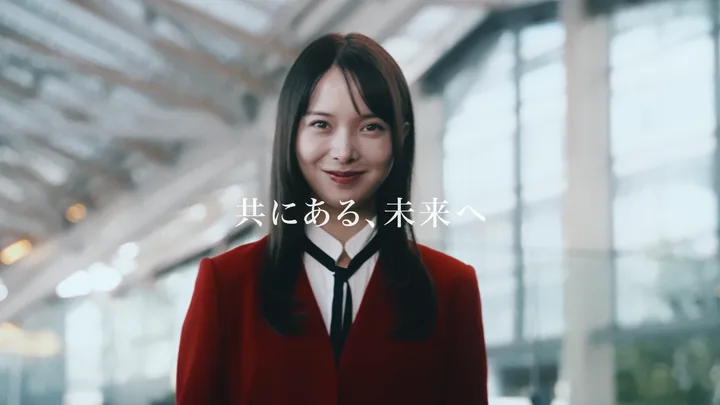 A woman in a red blazer smiling, with the line 「共にある、未来へ」