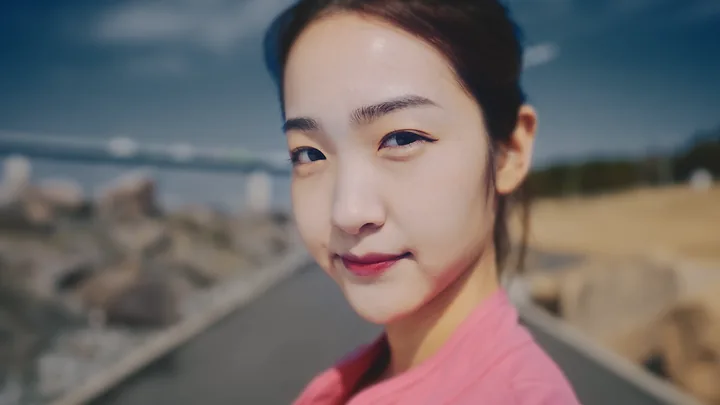 A young woman in pink looking into the camera by the sea