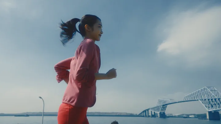 A woman in pink running along the waterfront under a bridge
