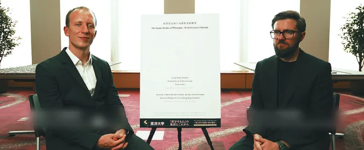 Two architects seated either side of the exhibition board