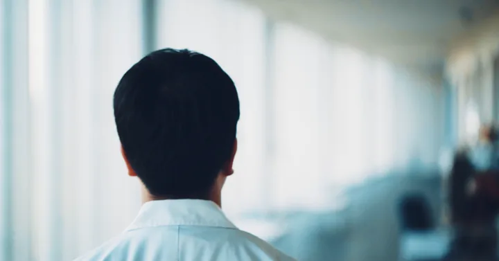 A student in a white shirt seen from behind in a bright hallway