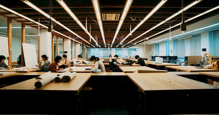 Students at drafting tables in a long, lit design studio